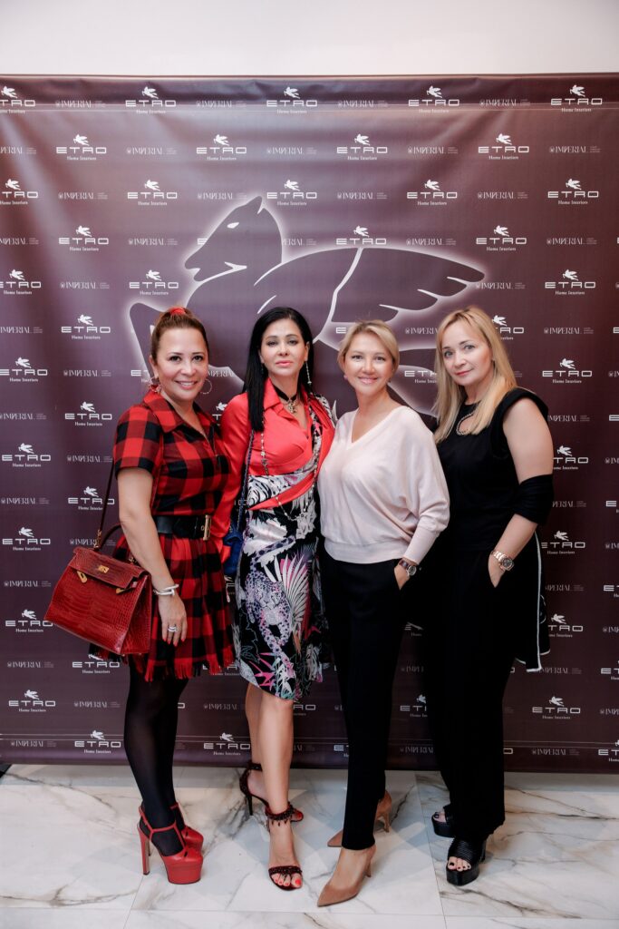Four guests at an event dedicated to the Etro collection presentation, posing in front of a branded backdrop